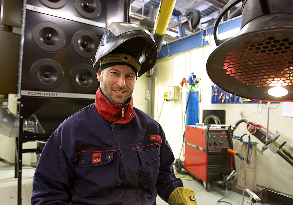 A man in a work shop smiling with protective gear on.